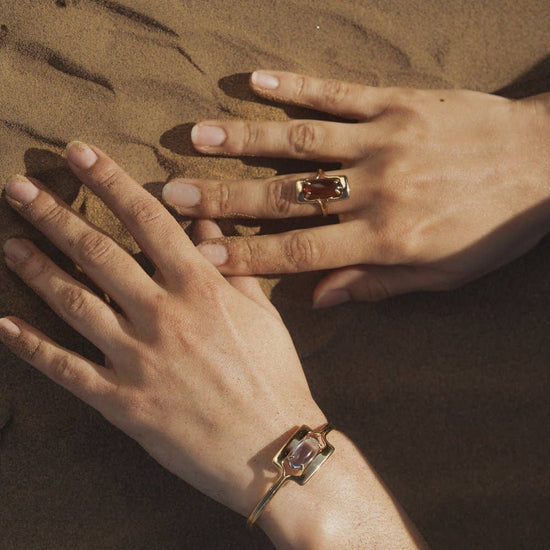 model wearing the amber walton ring on right middle finger and the blue walton cuff bracelet on their left wrist with their hands in sand