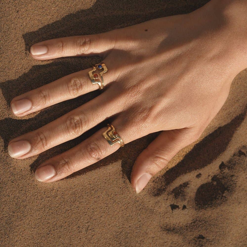 close up of a hand model wearing the grand ring on pointer finger with their hand in the sand and two other rings stacked on their ring finger