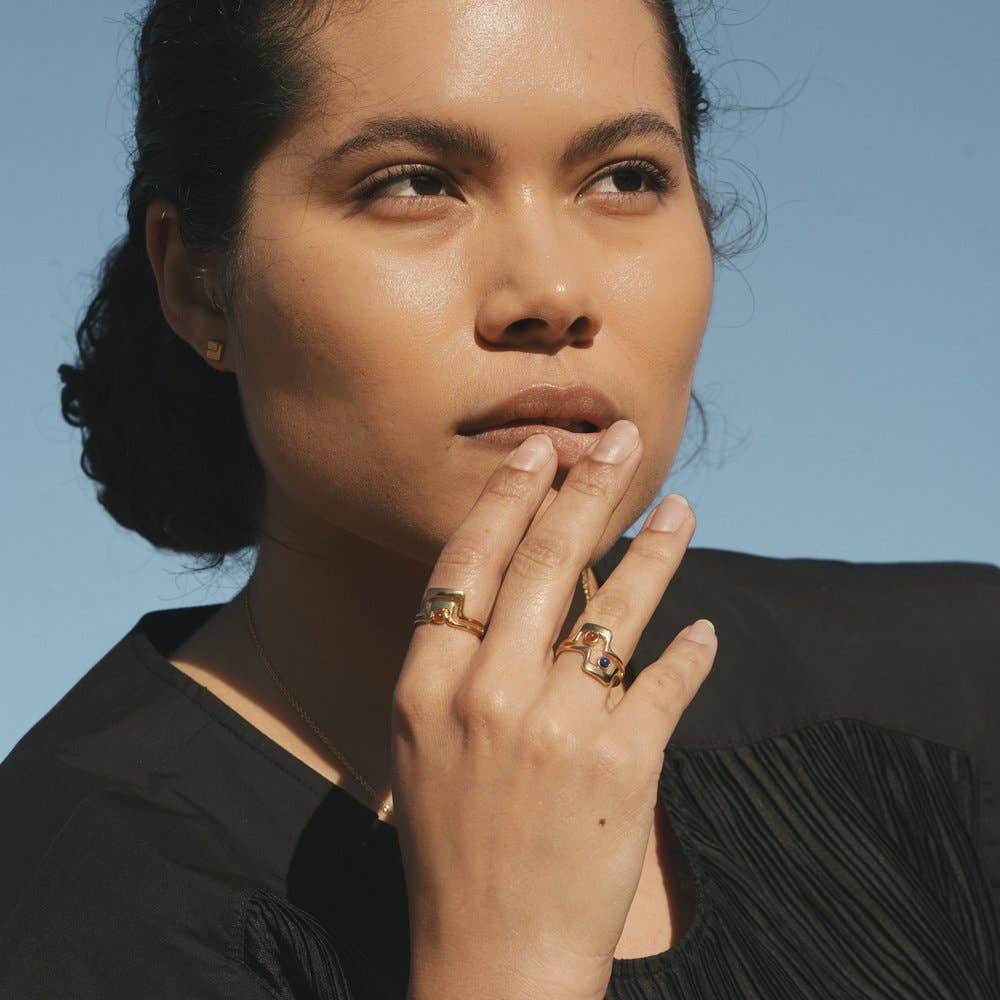 model wearing the grand ring on their pointer with two rings stacked on their ring finger with their hand by their face