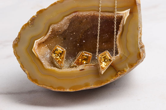 soleil necklace and stud earrings on an amber colored geode with a white background