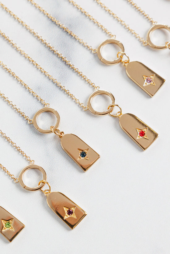 angled view of multiple iris birthstone charm necklaces on a beige background