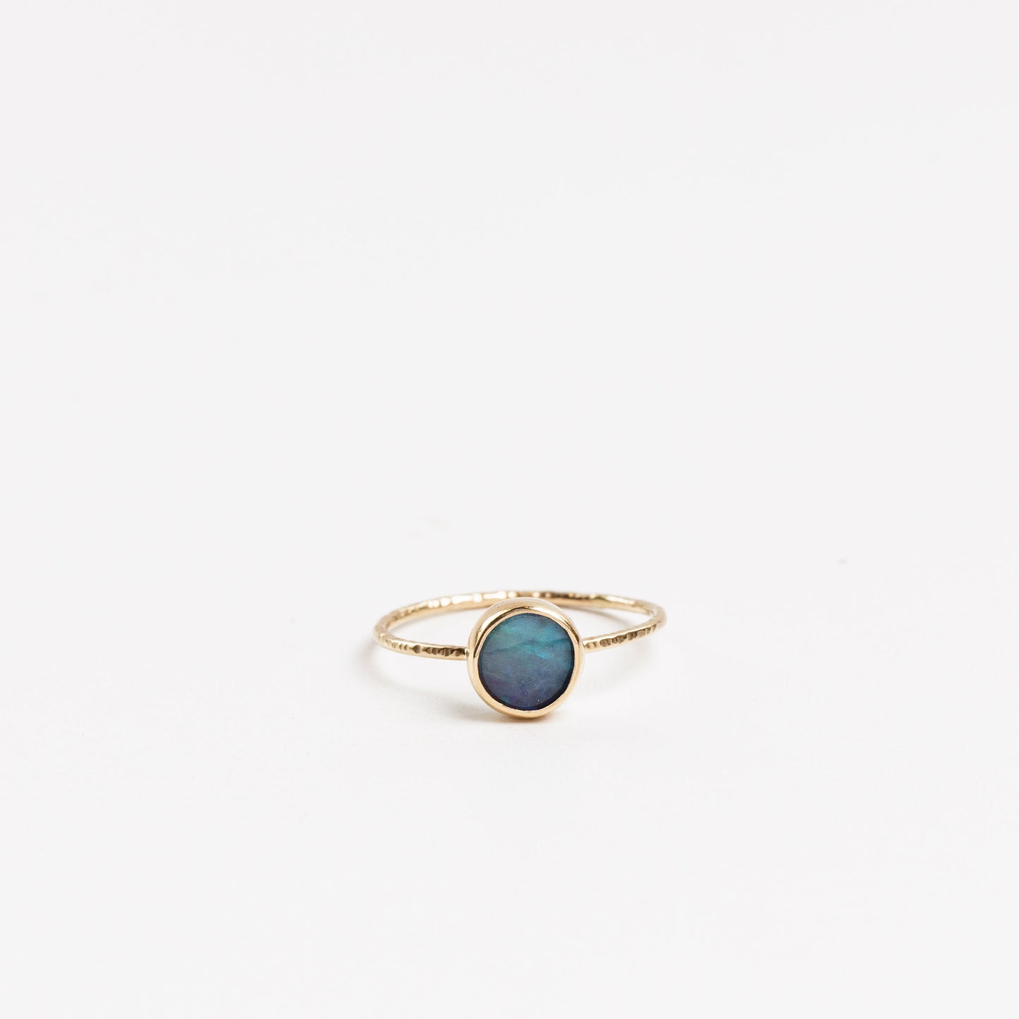 gold textured band ring with bezel set round blue opal on a white background