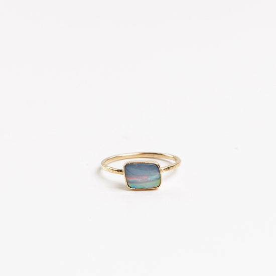asymmetrical square shaped opal bezel set on a gold band on a white background