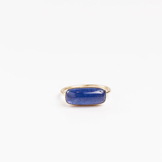 tanzanite cabochon bezel set in yellow gold on a white background