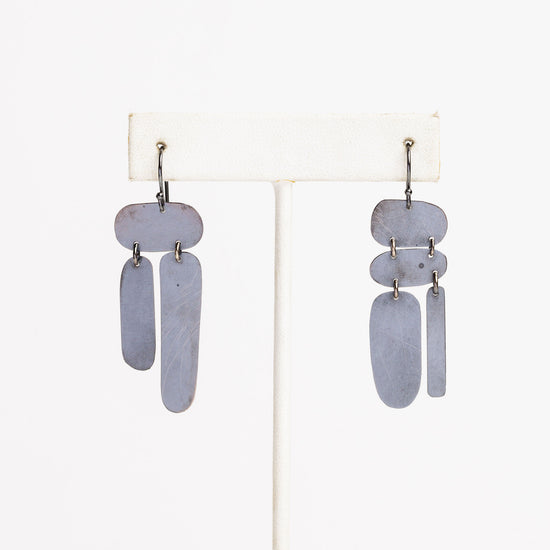 white earring stand with mismatched oxidized silver dandle earrings on a white background