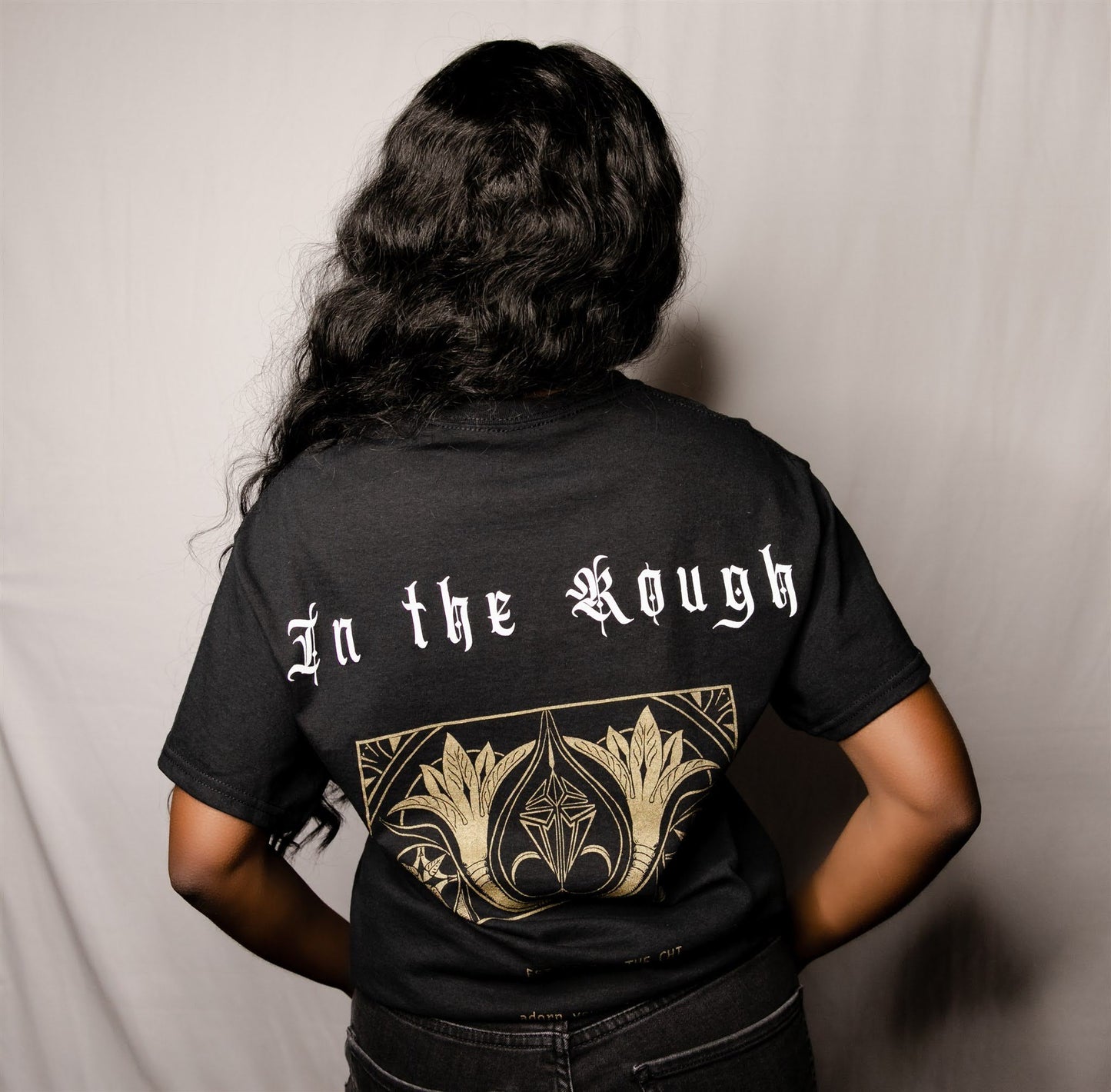 back view of a woman wearing the diamond in the rough tee shirt with a grey backdrop