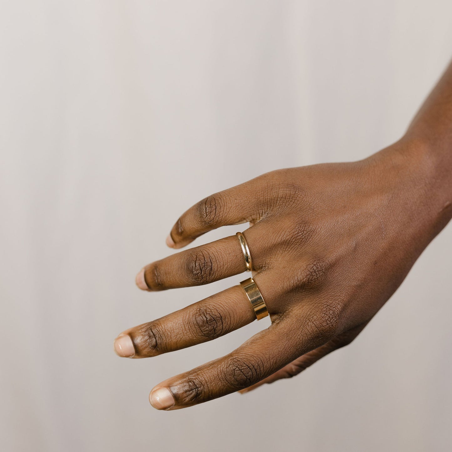 close up of a hand model wearing a large gold band on their right middle finger and a half round yellow gold band on their ring finger