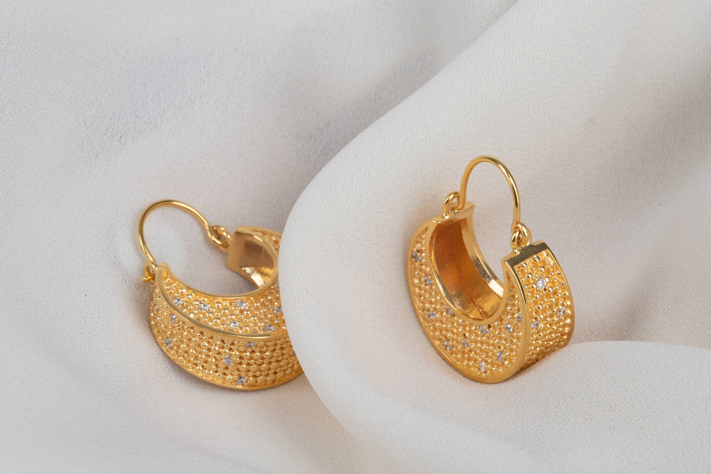 gold drop dot dangle hoop earrings on a grey fabric background