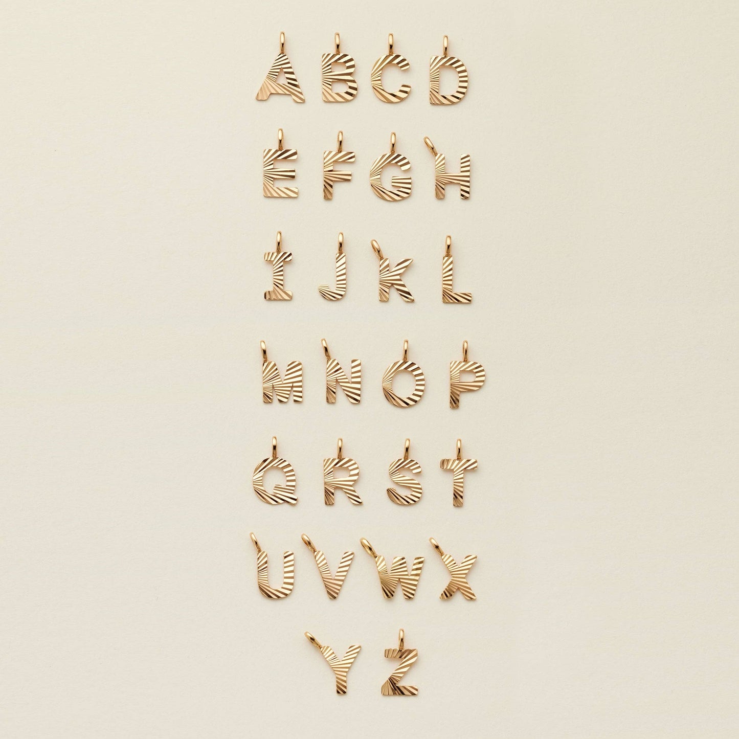textured gold initial charms displayed in alphabetical order a through z on a beige background