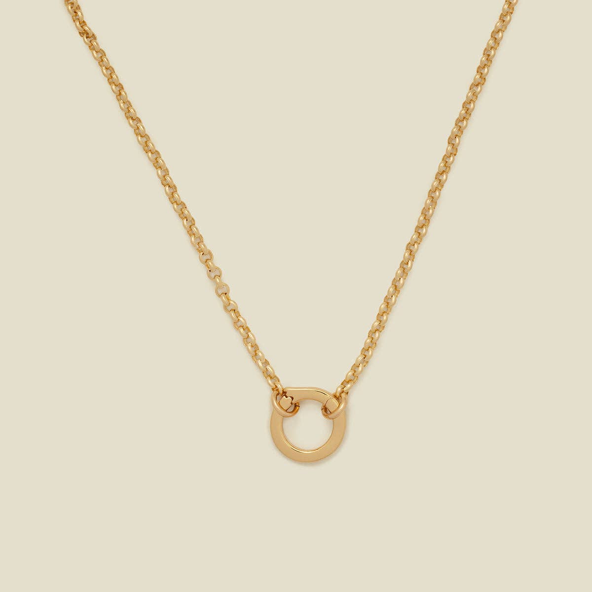 close up of a gold necklace with a circle lock charm and rolo chain on a beige background