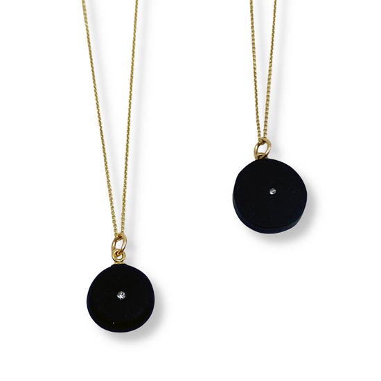 Two round black stone pendant necklaces with diamond accent on white background.