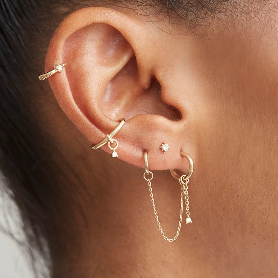 a close up of a model wearing the dala diamond stud in her second ear piercing with four gold hoops with chain and diamond details in her other piercings