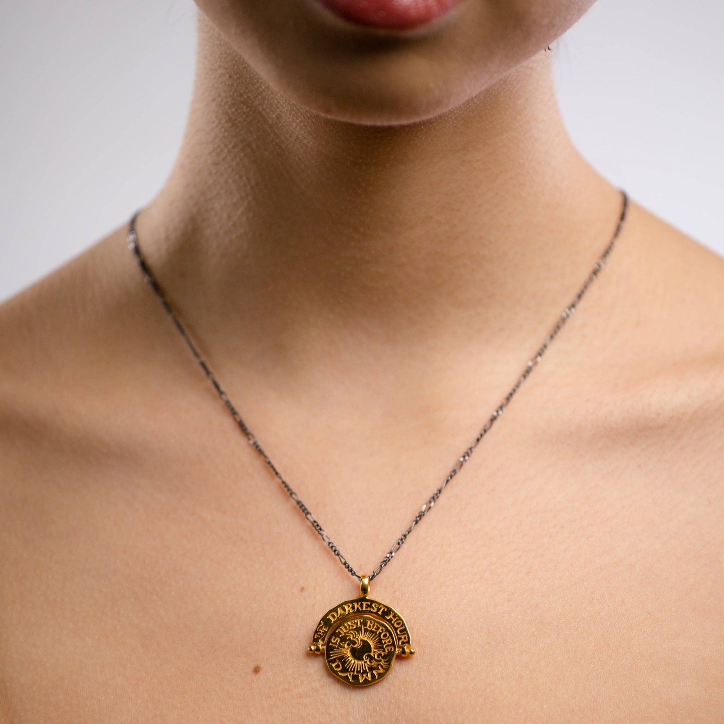 Necklace with a gold pendant worn by a person on a neutral background