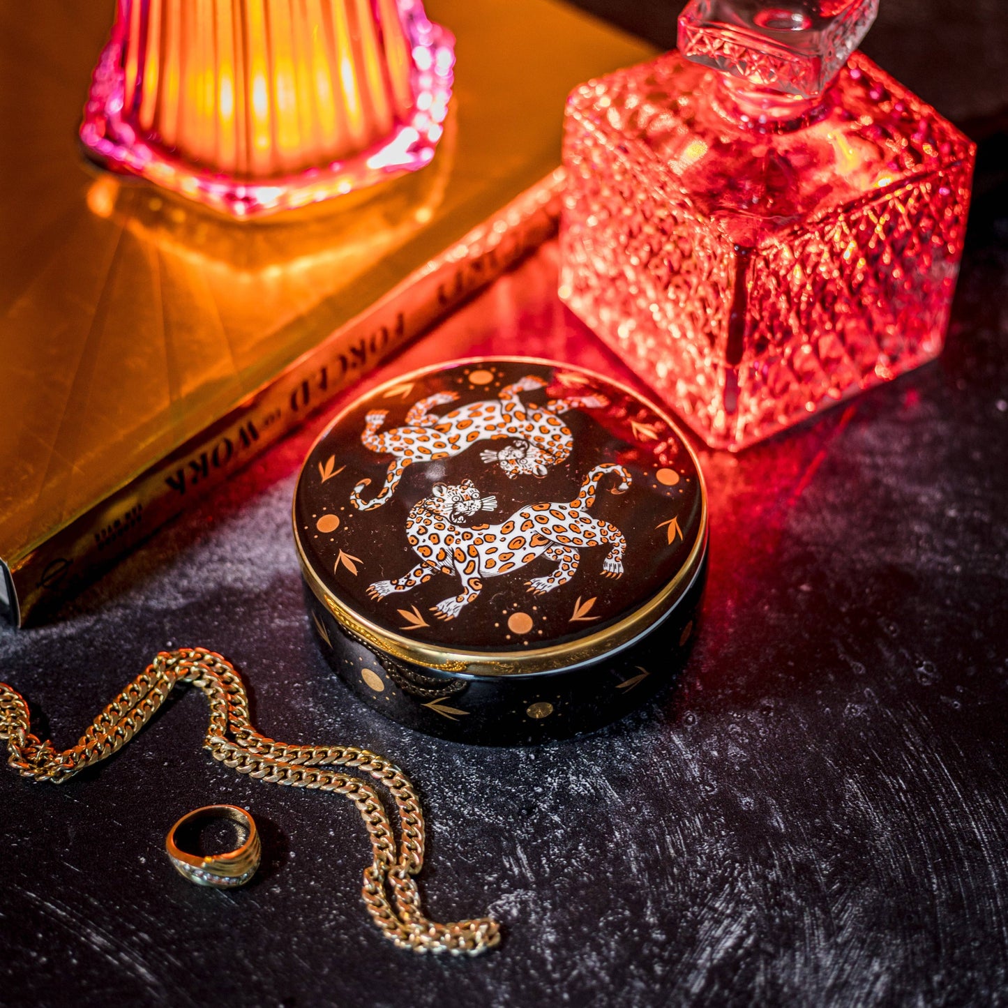 the leopard trinket box on a black table with jewelry, and orange glass, and light