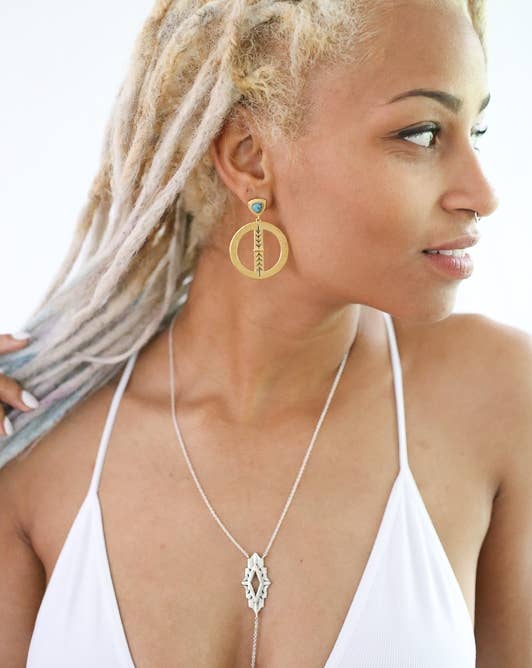 Woman wearing gold hoop earrings and a silver necklace against a white background