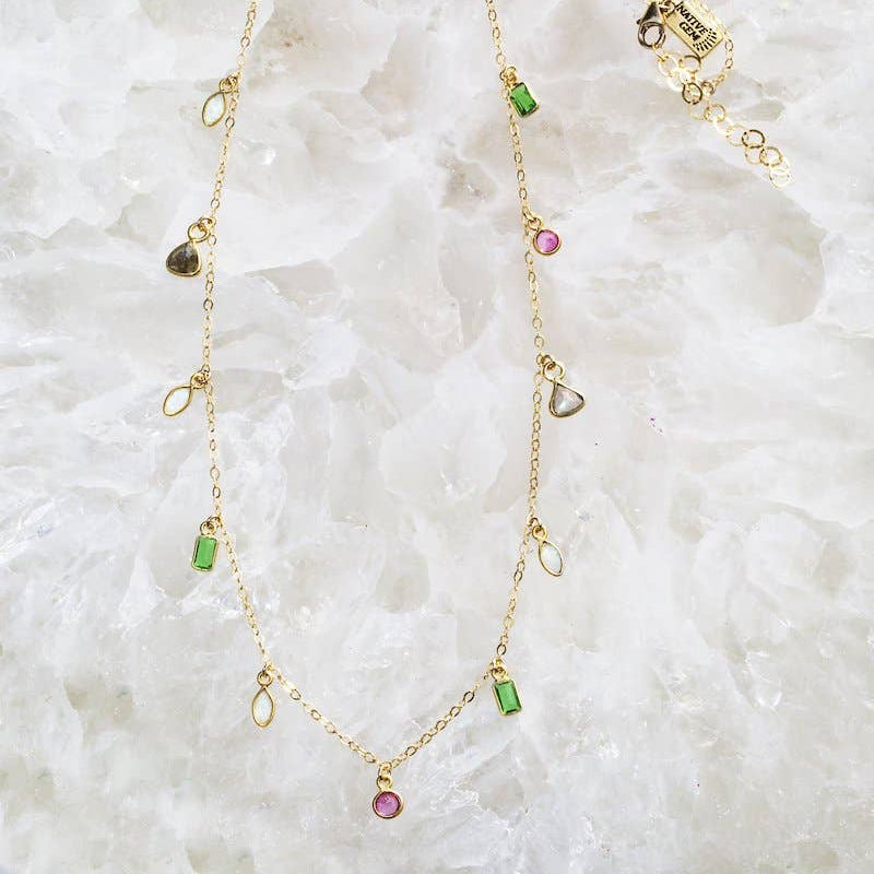 Gold necklace with gemstones on a textured white surface