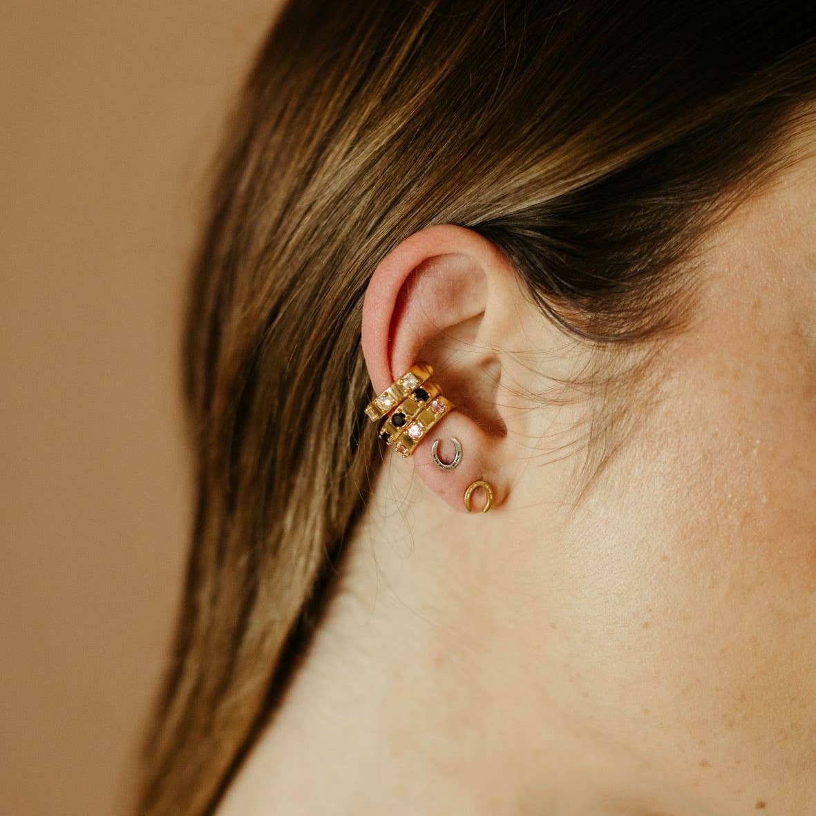 Close-up of an ear with gold earrings against a beige background