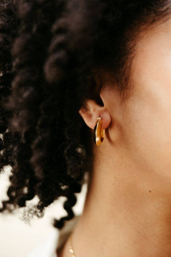 Close-up of a person wearing a gold hoop earring with dark hair.