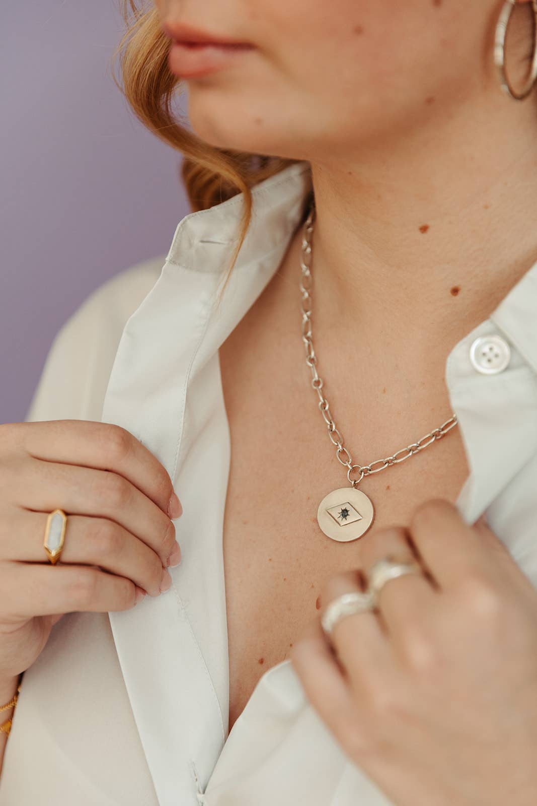 Person wearing a gold necklace with heart-shaped pendants, holding a ring.