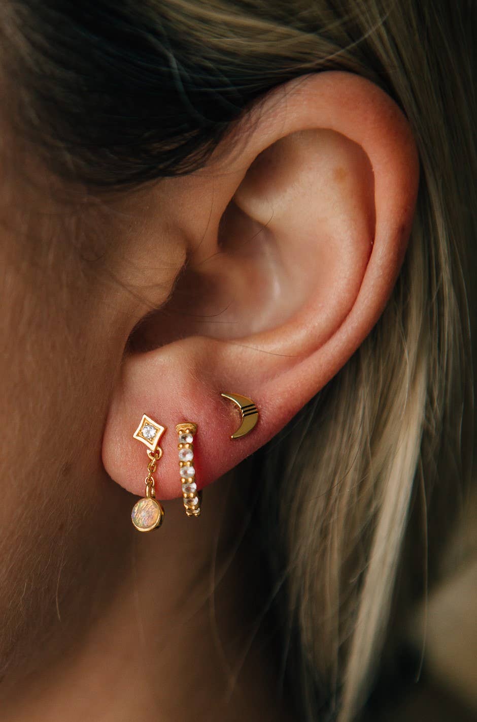 Close-up of an ear wearing gold earrings with a blurred background