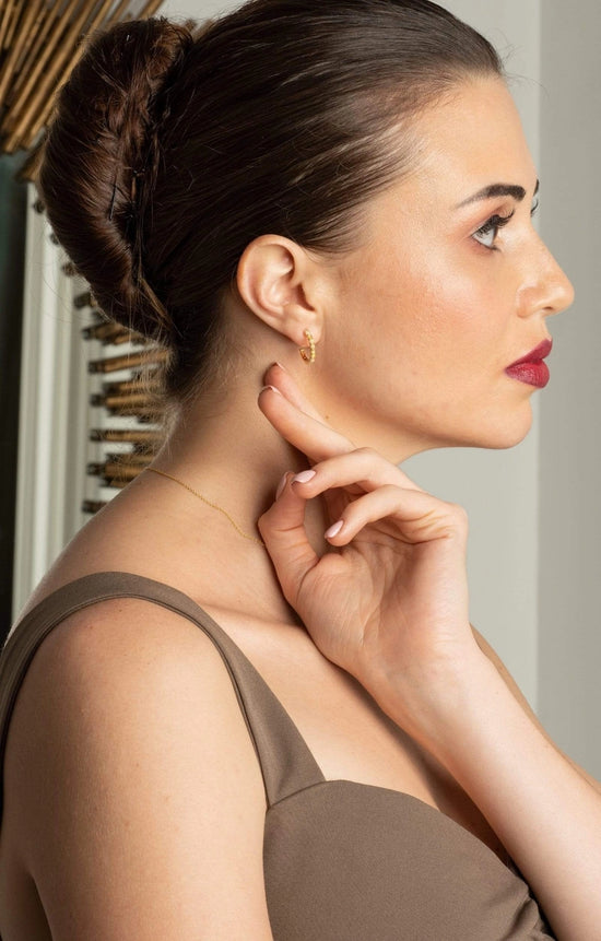 Woman wearing a gold earring, looking to the side with a neutral background