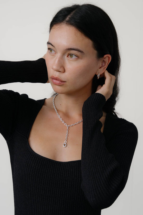 Woman wearing a black sweater and silver necklace against a white background