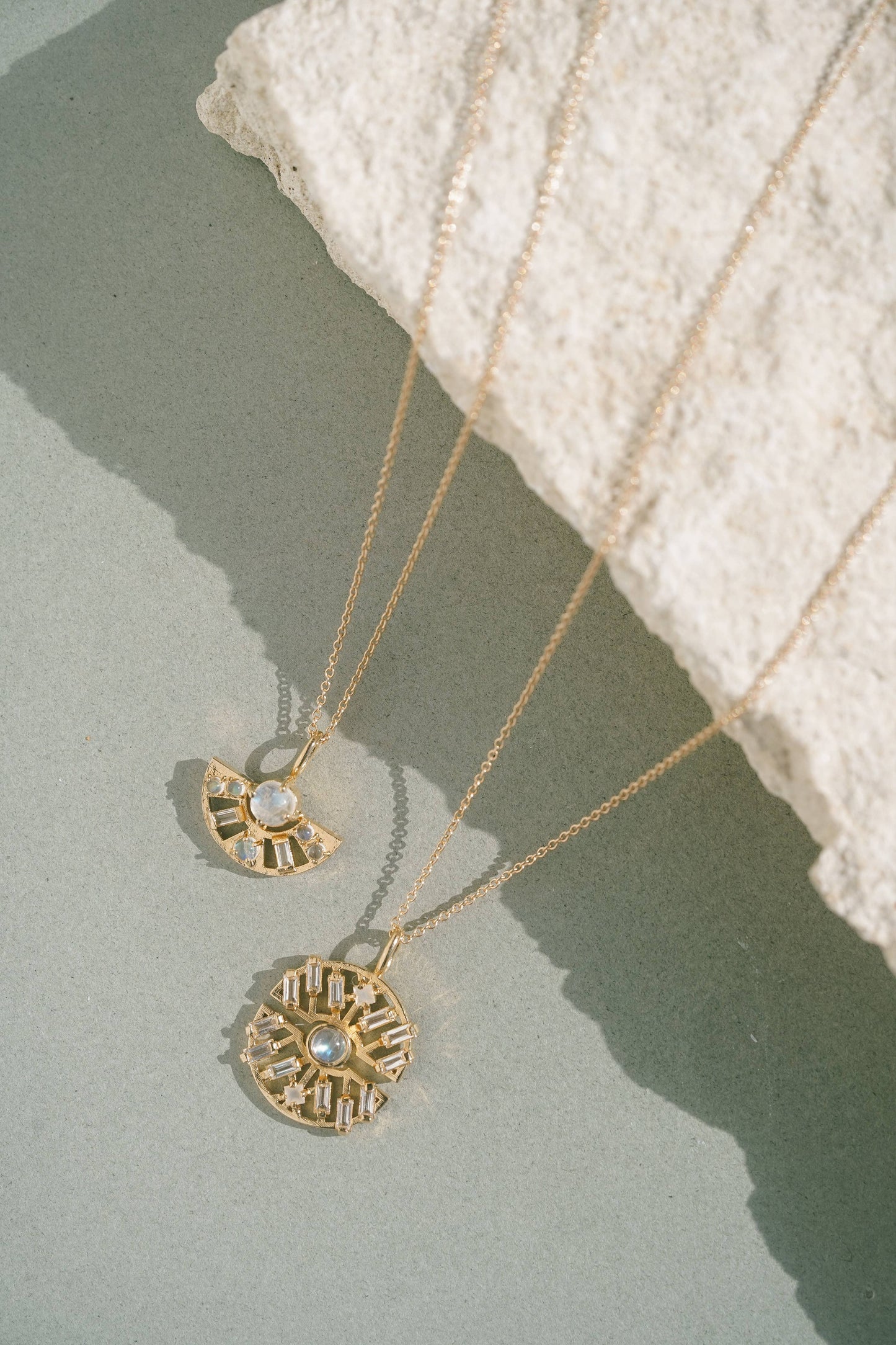 Two gold necklaces with pendants on a textured surface