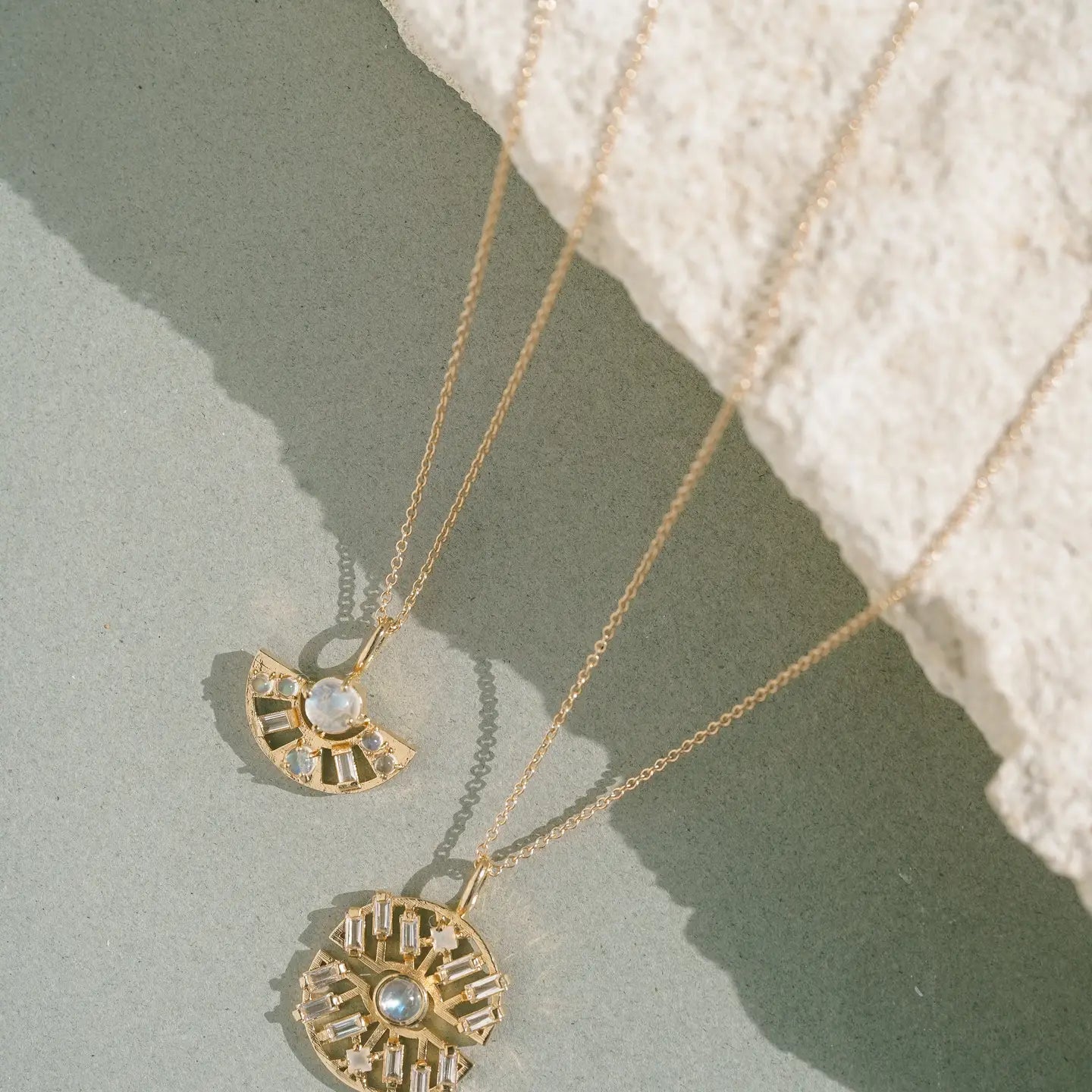 Two gold necklaces with pendants on a textured surface
