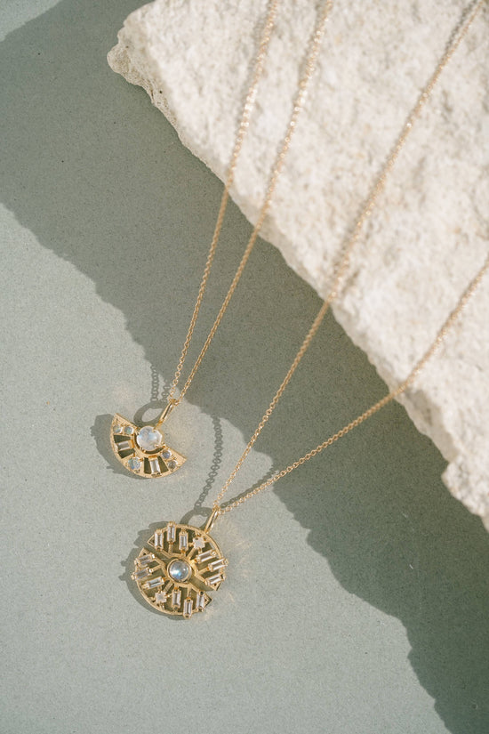 Two gold necklaces with pendants on a textured surface