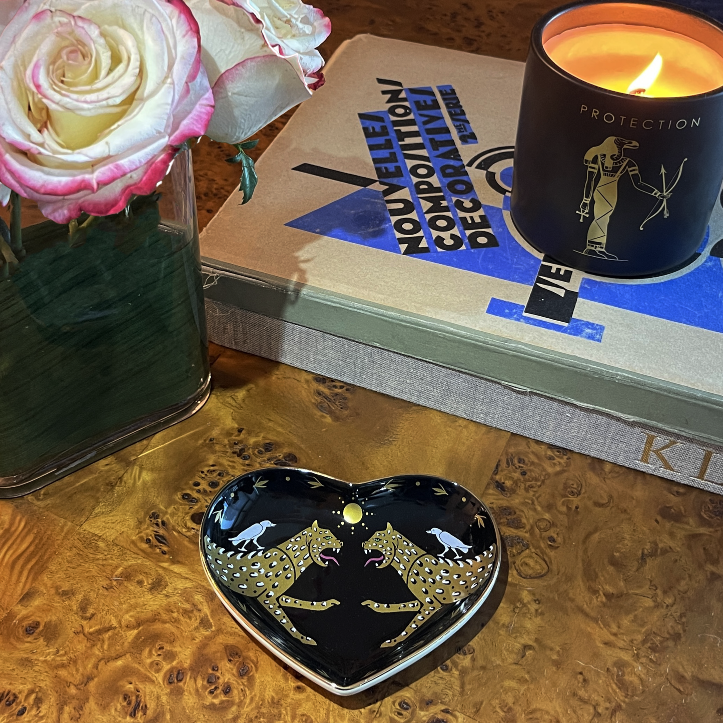 cheetah heart dish on a wood table with a candle on two books and a vase of roses