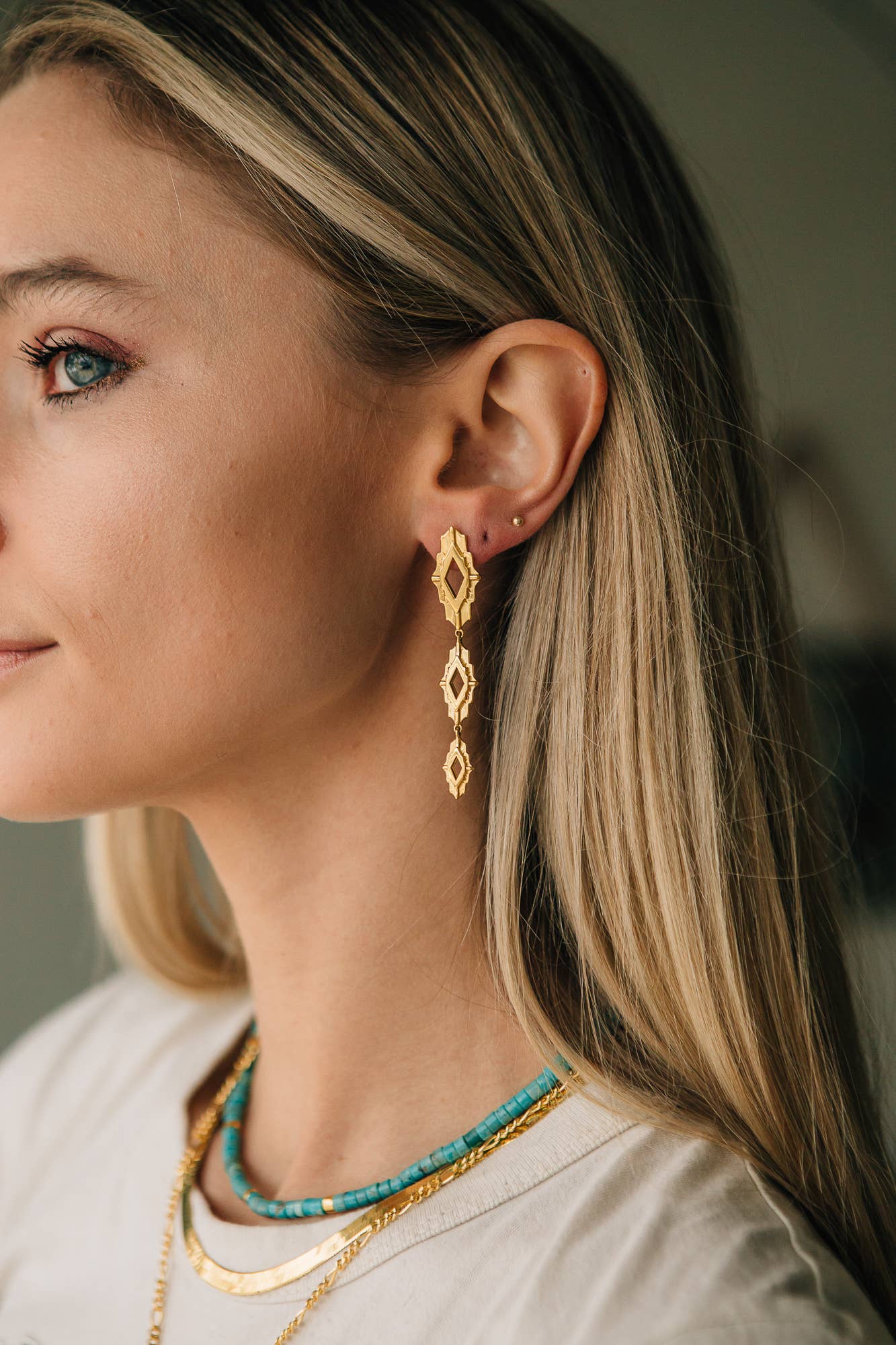 Close-up of a woman wearing gold earrings and a necklace with a blurred background