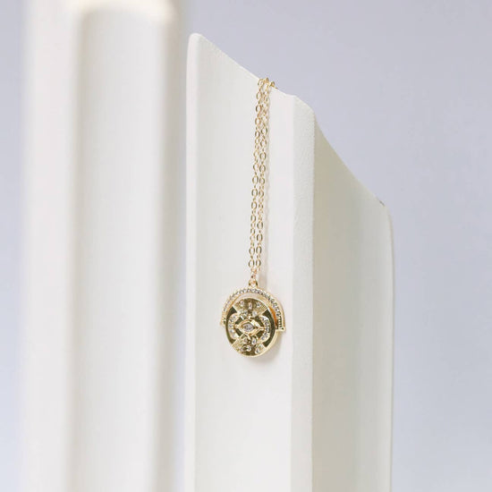 Gold necklace with a pendant on a white stand against a light gray background