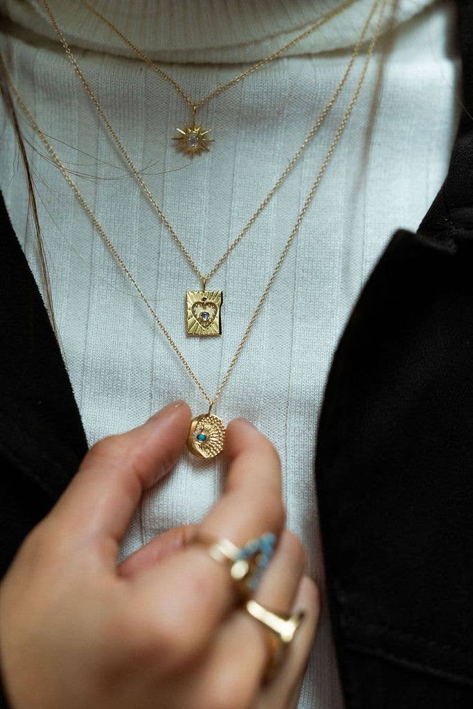 Close-up of a person wearing multiple gold necklaces with pendants on a light background