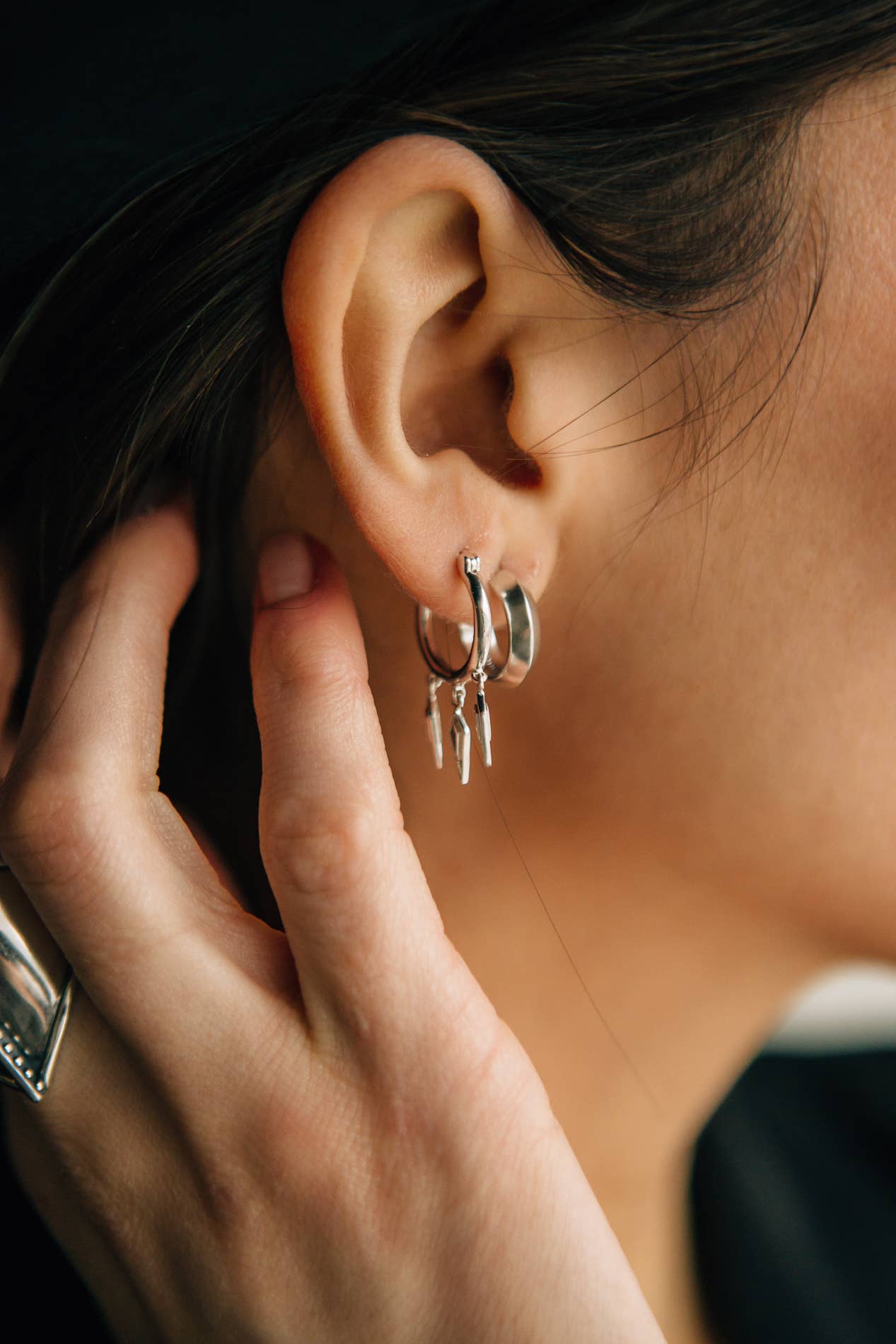 Close-up of an ear with a silver hoop earring, hand adjusting it.
