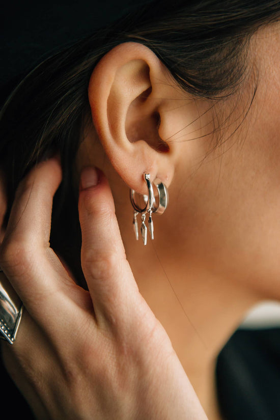 Close-up of an ear with a silver hoop earring, hand adjusting it.