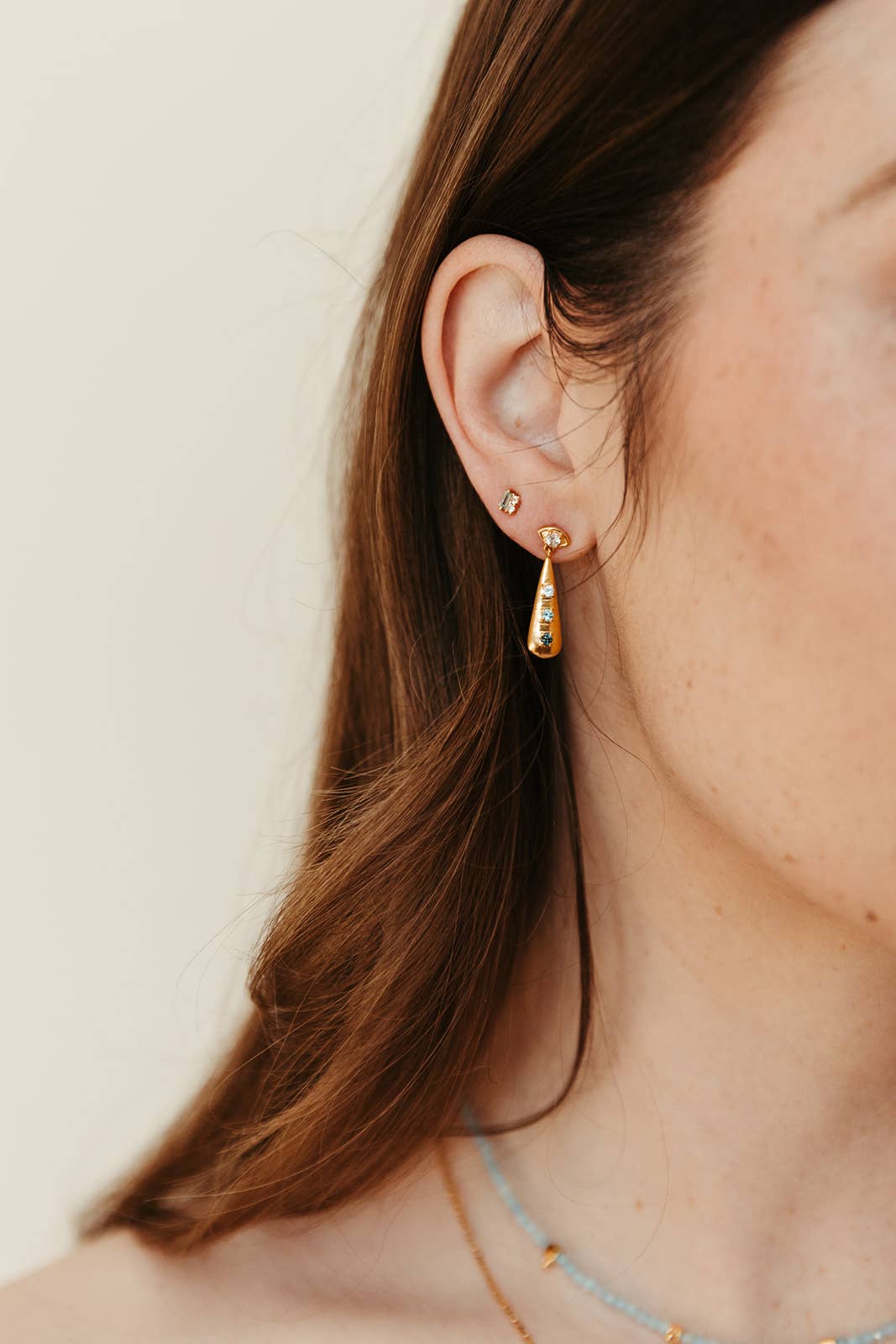 Close-up of a person wearing gold DROP earrings with a neutral background