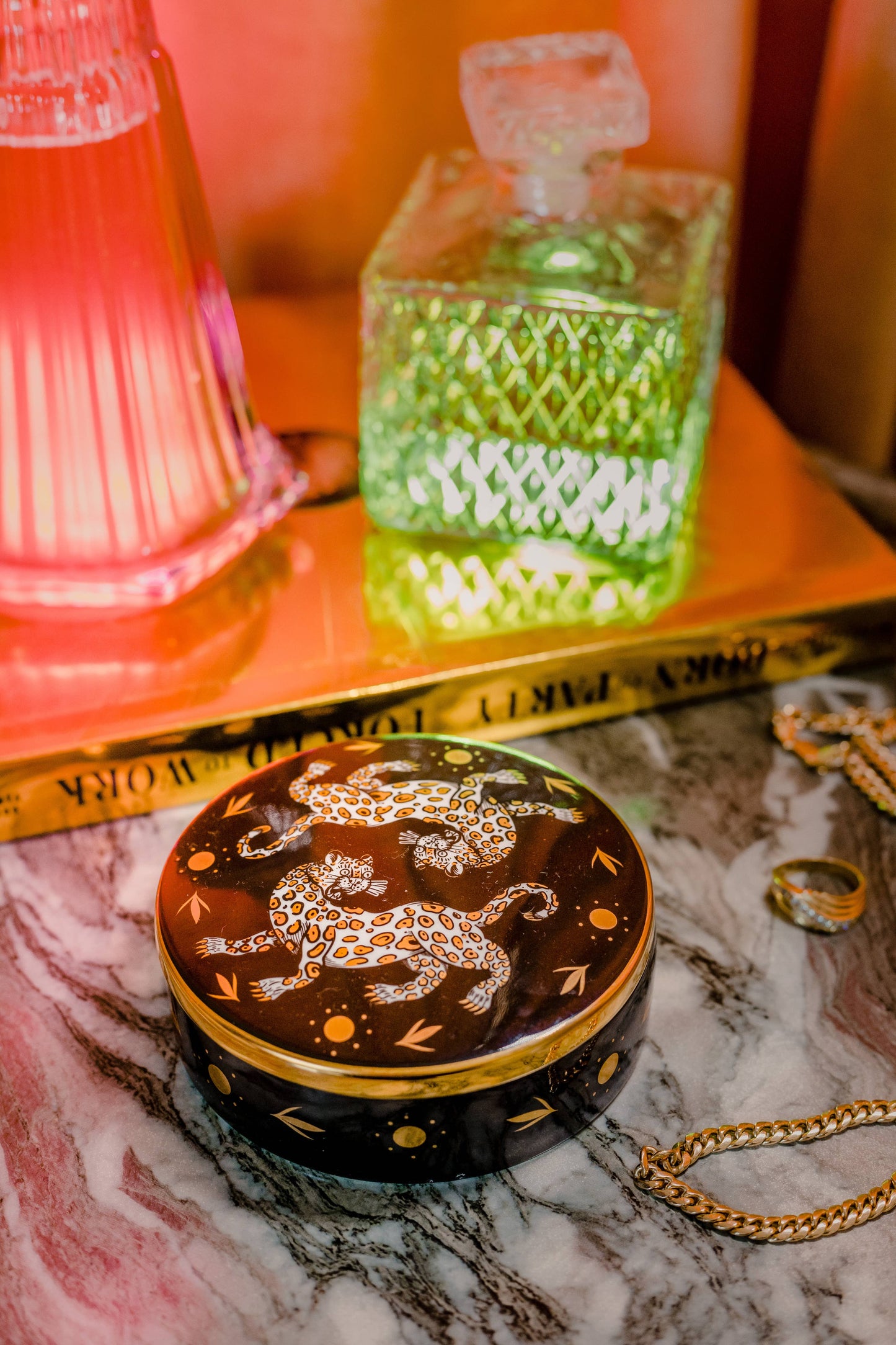 the leopard trinket box on a marble table with jewelry, a green glass, and orange light