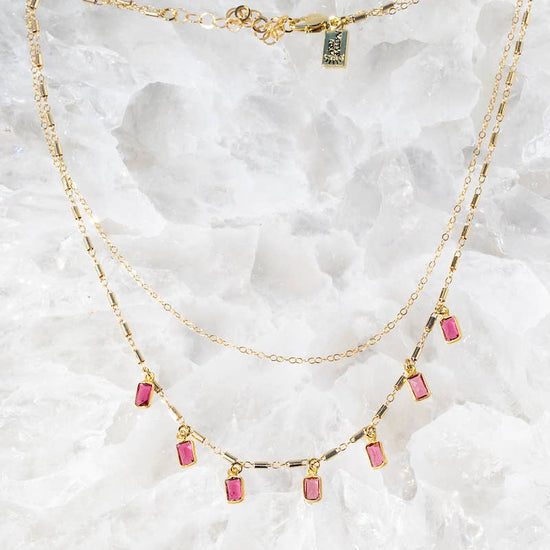 Gold necklace with pink gemstones on a white marble background