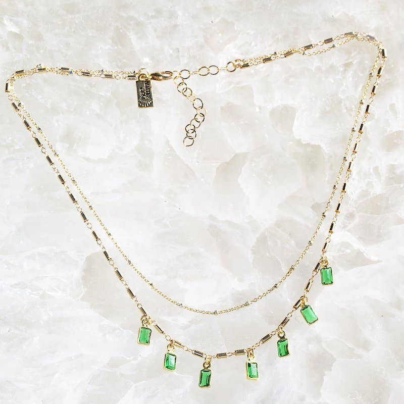 Gold necklace with green gemstones on a white marble background