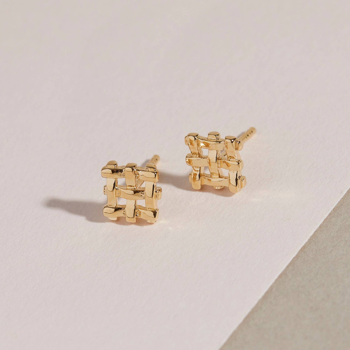 a pair of the crosshatch gold studs on a beige background