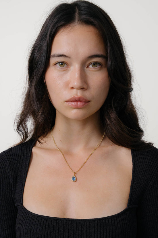 Woman wearing a necklace with a pendant against a plain background