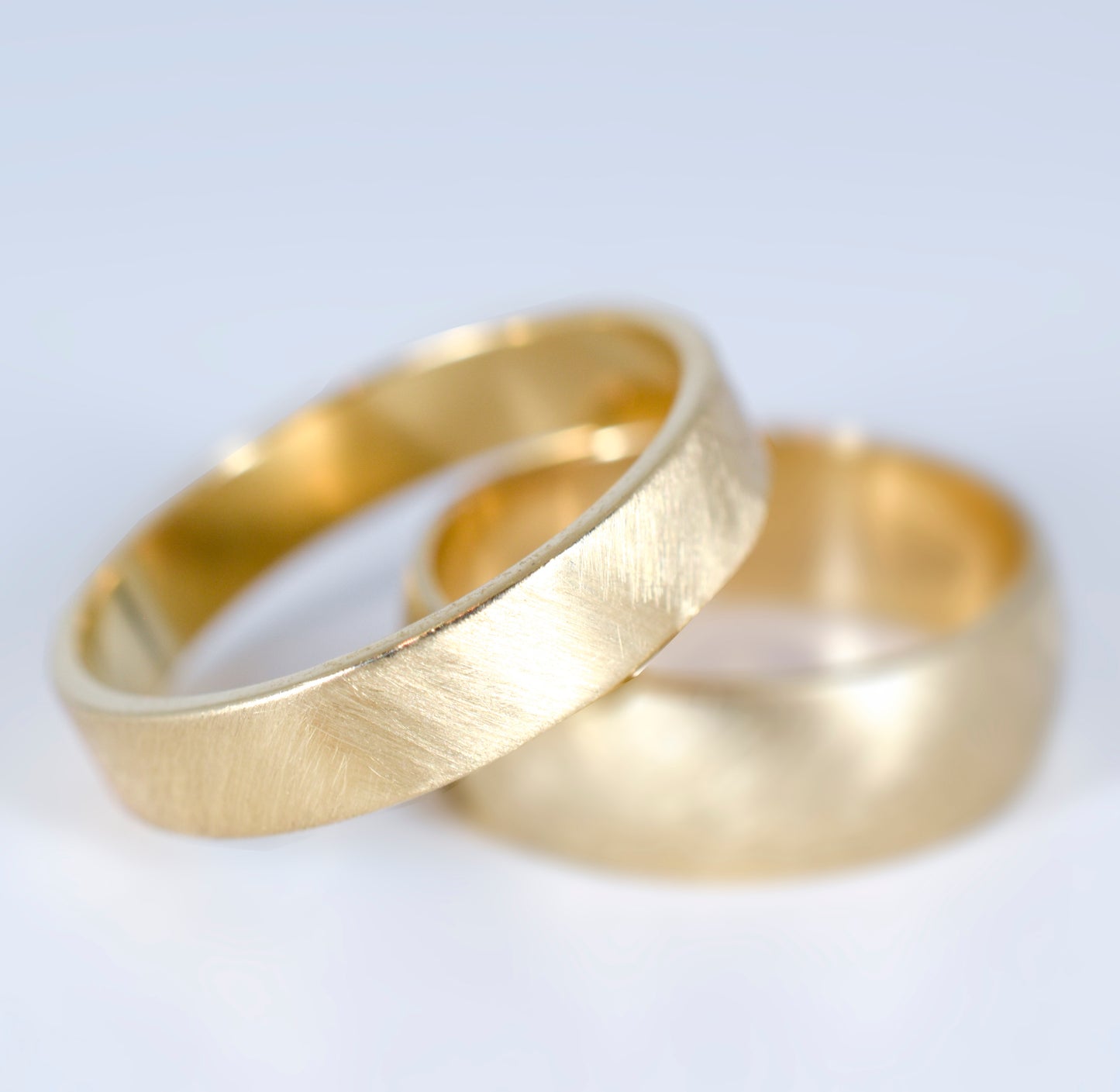 two yellow gold bands with a brushed textured finish stacked together with on in focus and one out of focus on a grey background