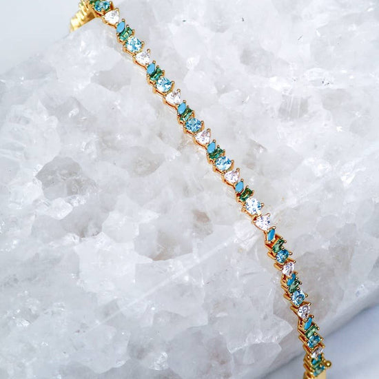 Gold bracelet with blue gemstones on a white crystal background