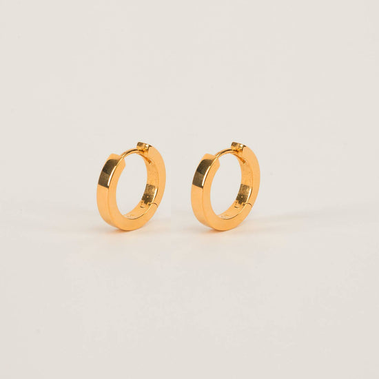 classic small gold huggie hoop earrings on a beige background