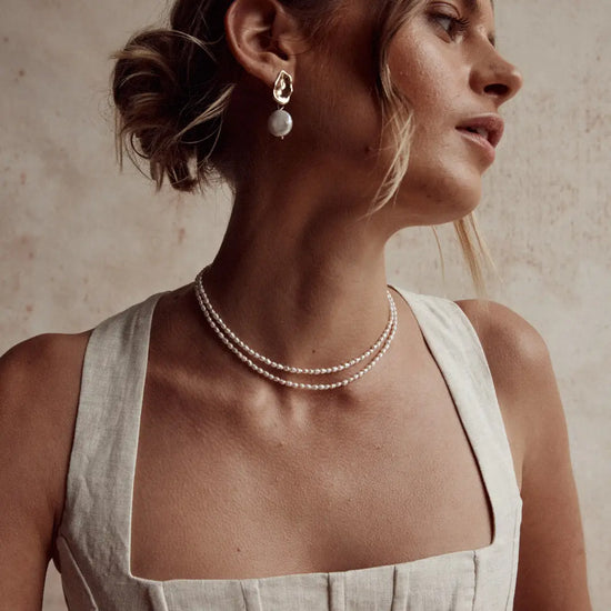 model wearing two of the delicate pearl necklaces and a pair of gold pearl earrings