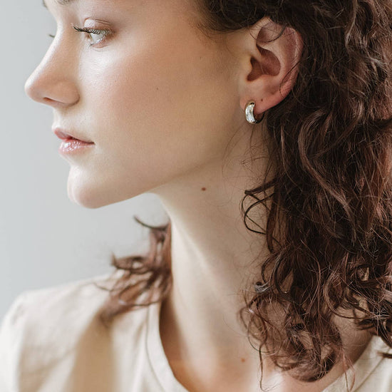 Close-up of a woman wearing a silver earring with a neutral background