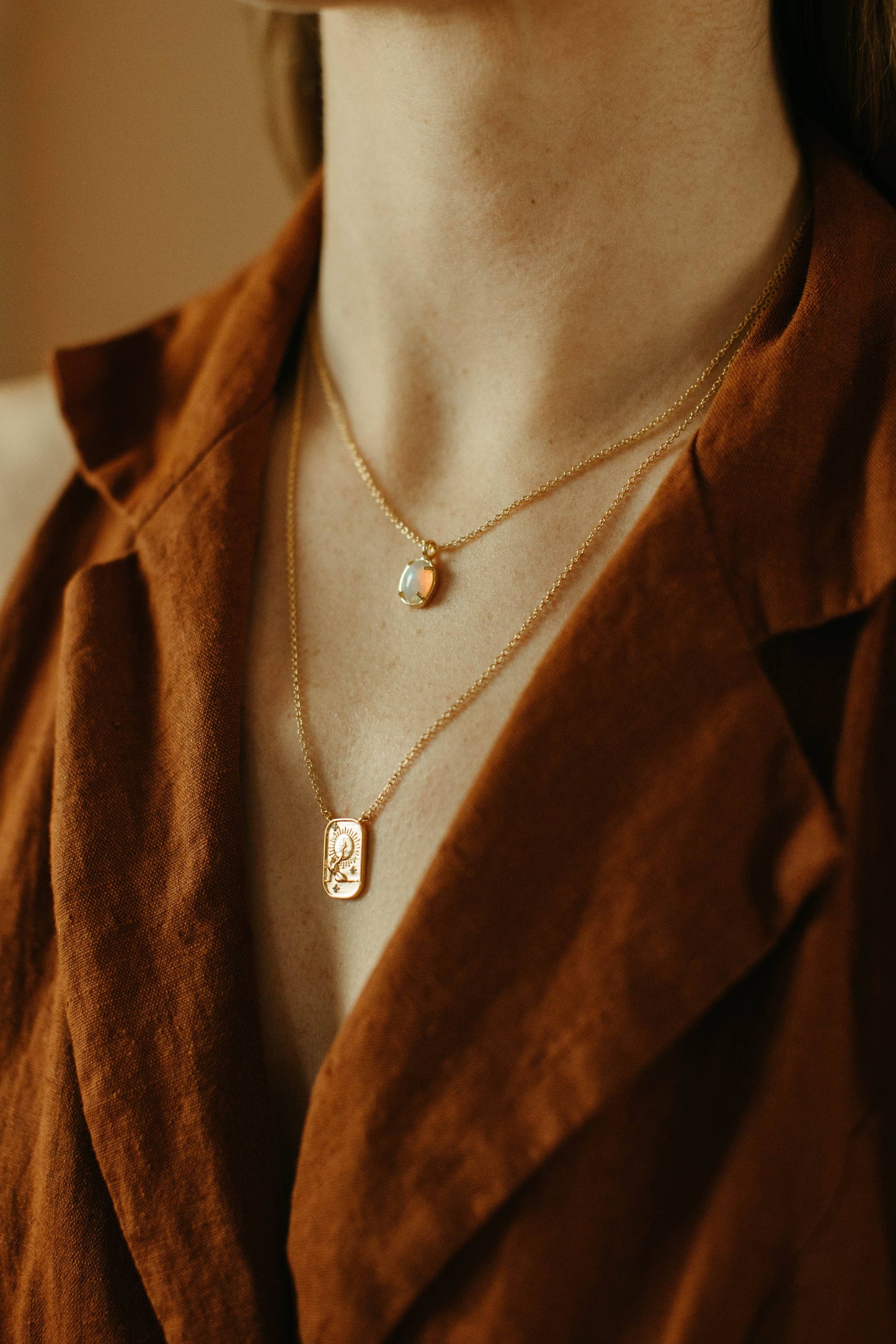 Necklace with pendant worn by a person in a brown jacket.
