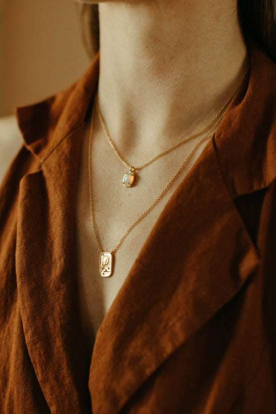Necklace with pendant worn by a person in a brown jacket.