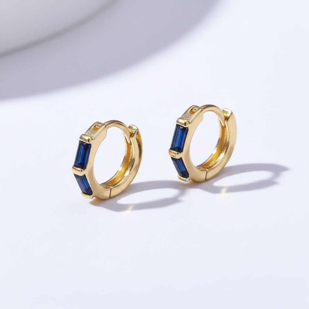 Gold hoop earrings with blue gemstones on a light purple background