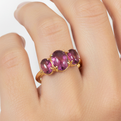 Gold ring with three pink gemstones on a white background